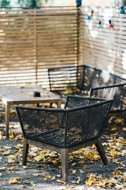 A small garden patio featuring two ornate black metal chairs with intricate floral and scrollwork designs, positioned on either side of a matching round metal table with a decorative patterned surface